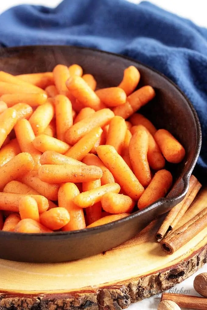 Maple glazed carrots in a cast iron skillet next to a blue linen.