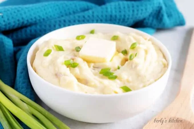 An angled picture of the mashed red potatoes in a serving bowl topped with butter and green onions.