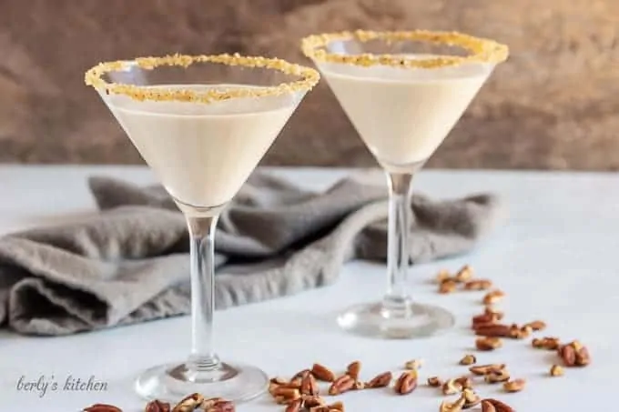 Two pecan pie martinis in martini glasses, rimmed with brown sugar and pecans.