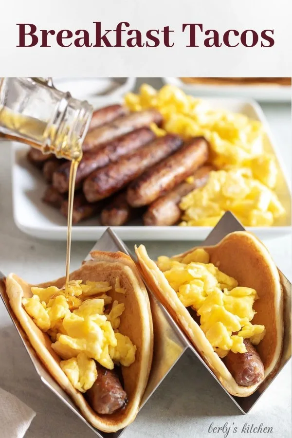 Two finished breakfast tacos with eggs and sausage, drizzled with maple syrup.