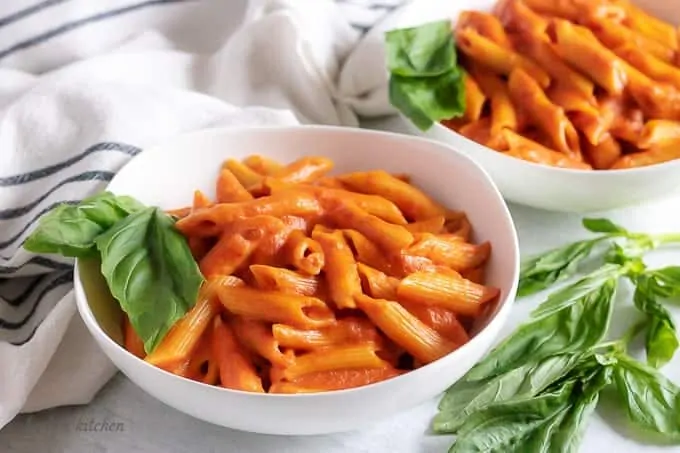 Two bowls of penne with vodka sauce and basil.