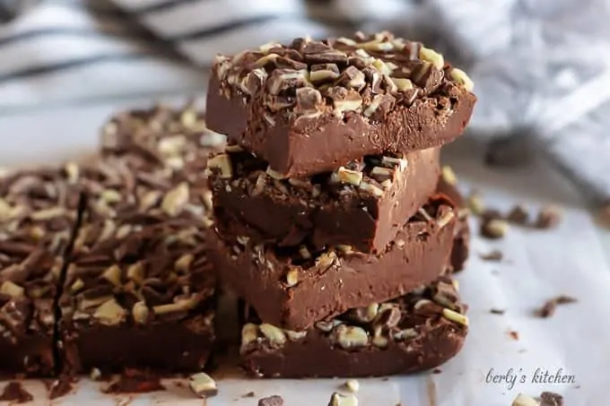 Multiple pieces of mint chocolate fudge stacked on a cutting board.