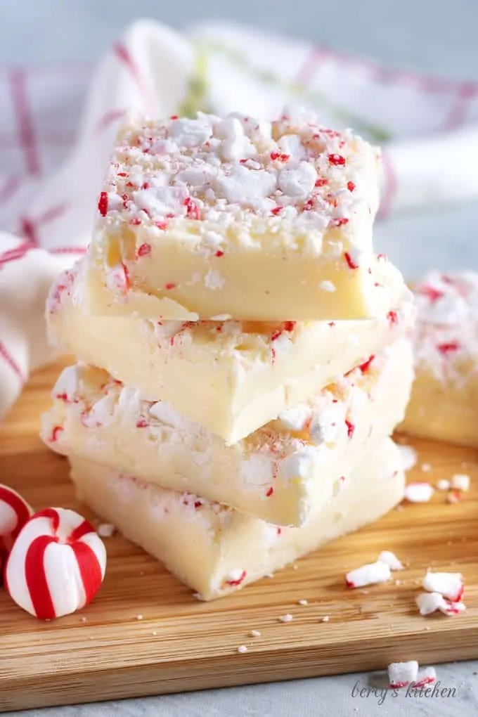 Four pieces of peppermint fudge stacked on a cutting board for presentation.