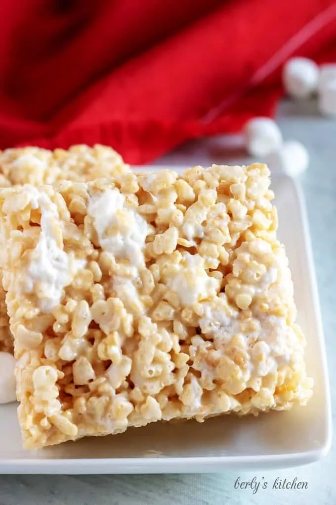 Two large rice krispie treats on a white plate next to a red napkin.