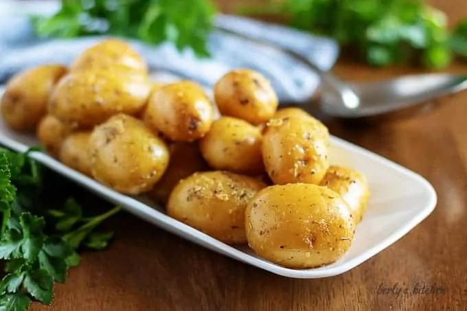 The baby potatoes, covered in butter, on a serving white plate.