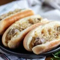 Three beer brats, in buns, topped with sauerkraut and onions.