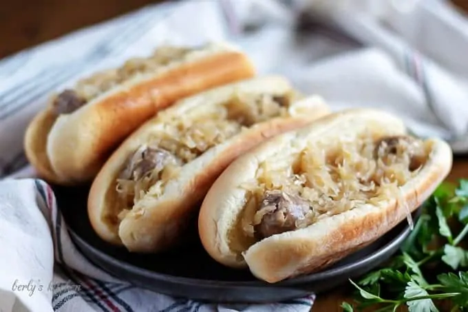 Three beer brats, in buns, topped with sauerkraut and onions.