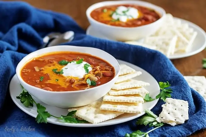 Two bowls of chili topped with cheese, green onions, and sour cream.