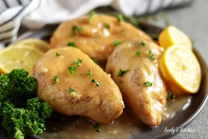 Three lemon chicken breasts, covered in sauce, and garnished with parsley.