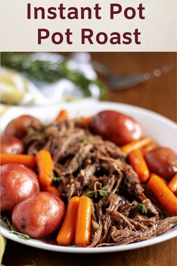 The pot roast on a platter surrounded by carrots and potatoes.