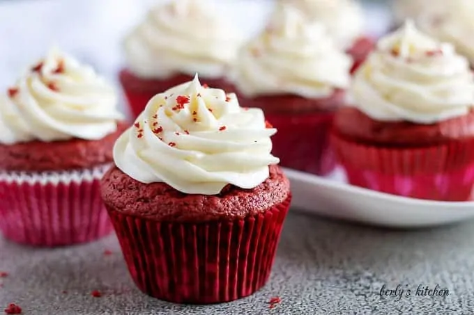 The finished red velvet cupcakes, in red liners, topped with frosting.