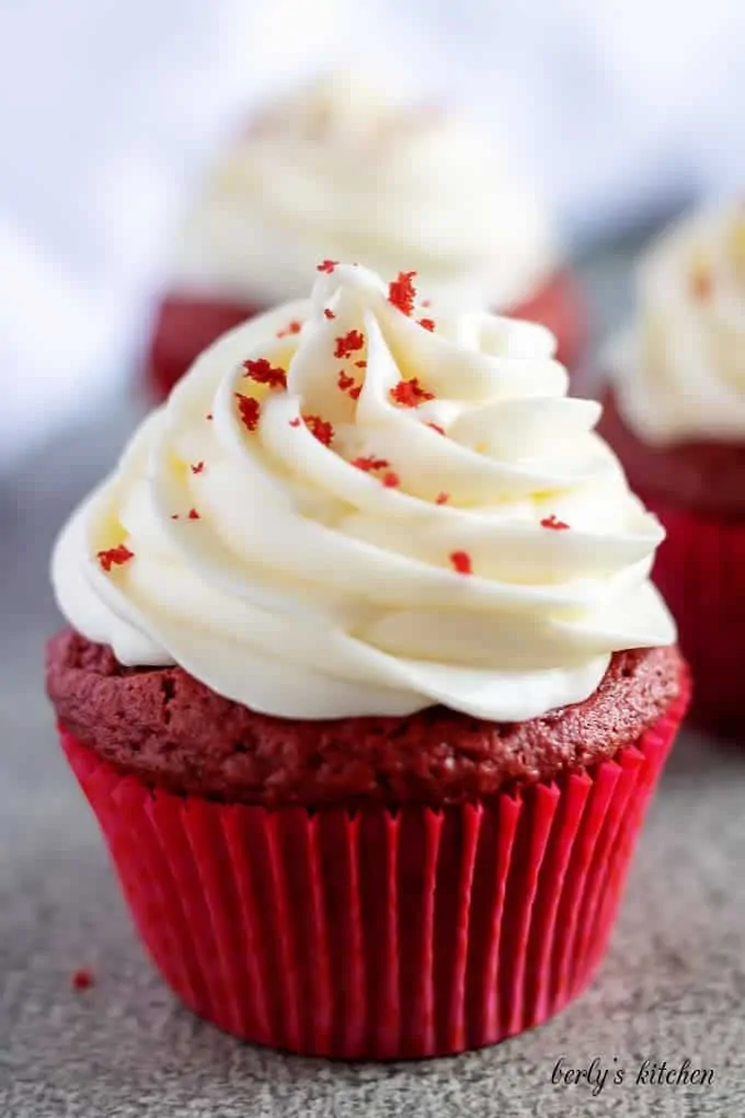 A red velvet cupcake, with cream cheese frosting, in a red liner.