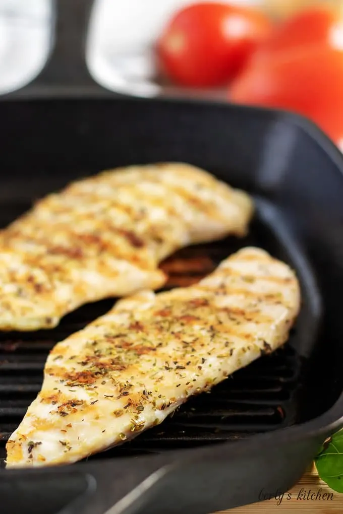 Two seasoned chicken breasts cooking in a black griddle pan.