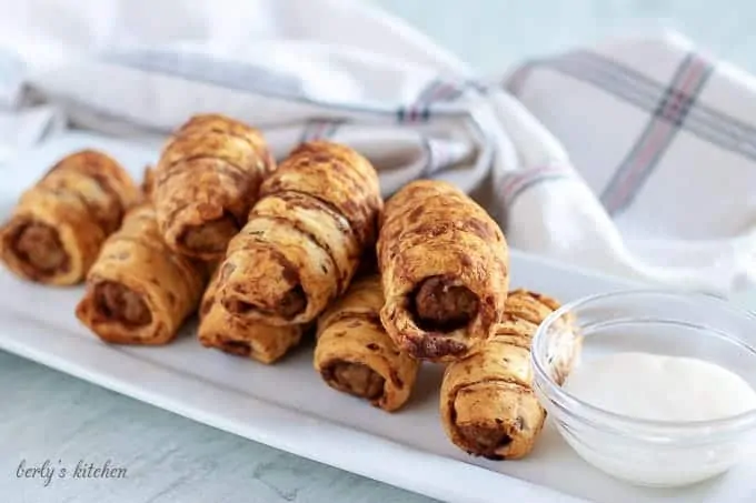 Seven pigs in a blanket on a rectangular serving dish with icing.