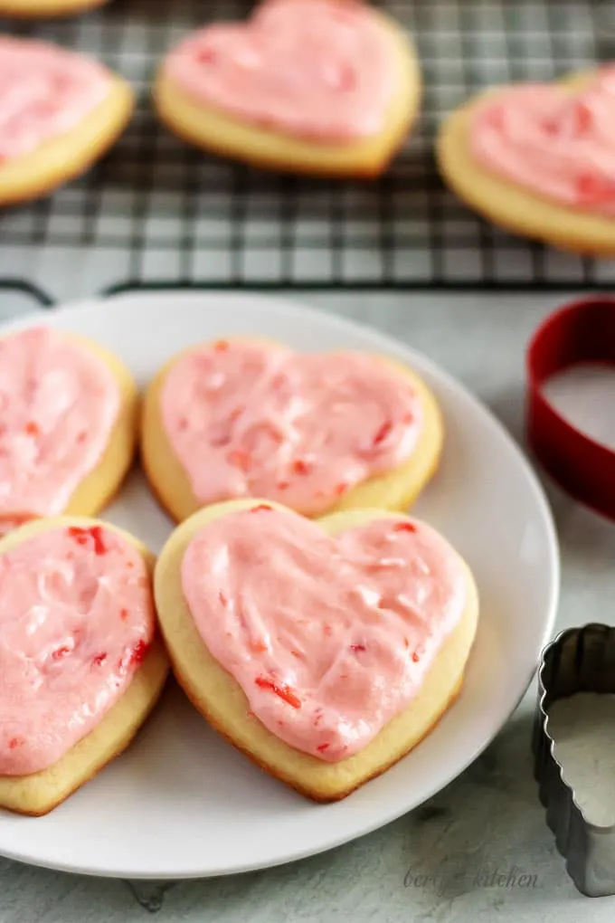 Cut out sugar cookies on a white plate next to a cooling rack.