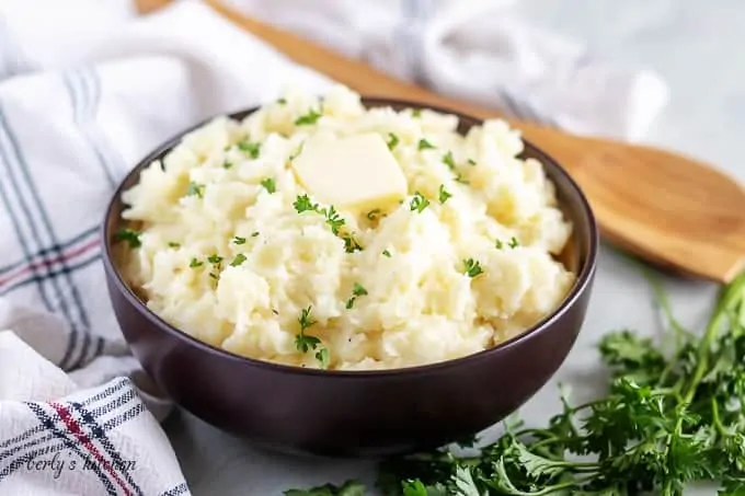 Garlic mashed potatoes in a brown bowl, topped with unsalted butter.