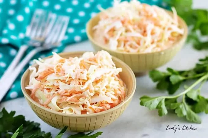 Two bowls of cream coleslaw with forks and a polka dot towel.