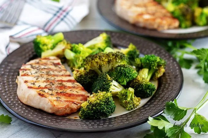 A grilled pork chop, on a plate, with a side of broccoli.