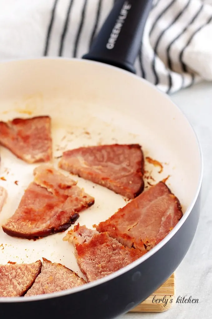 Seven slices of smoked ham seared in a large skillet.