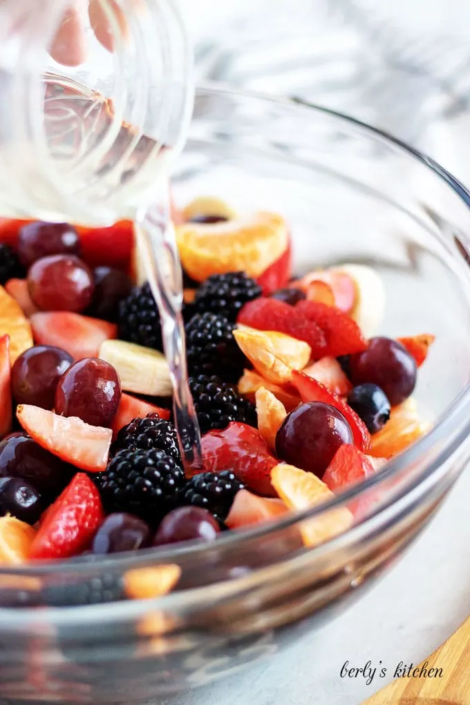 The lemon infused simple syrup being poured over the homemade fruit salad.