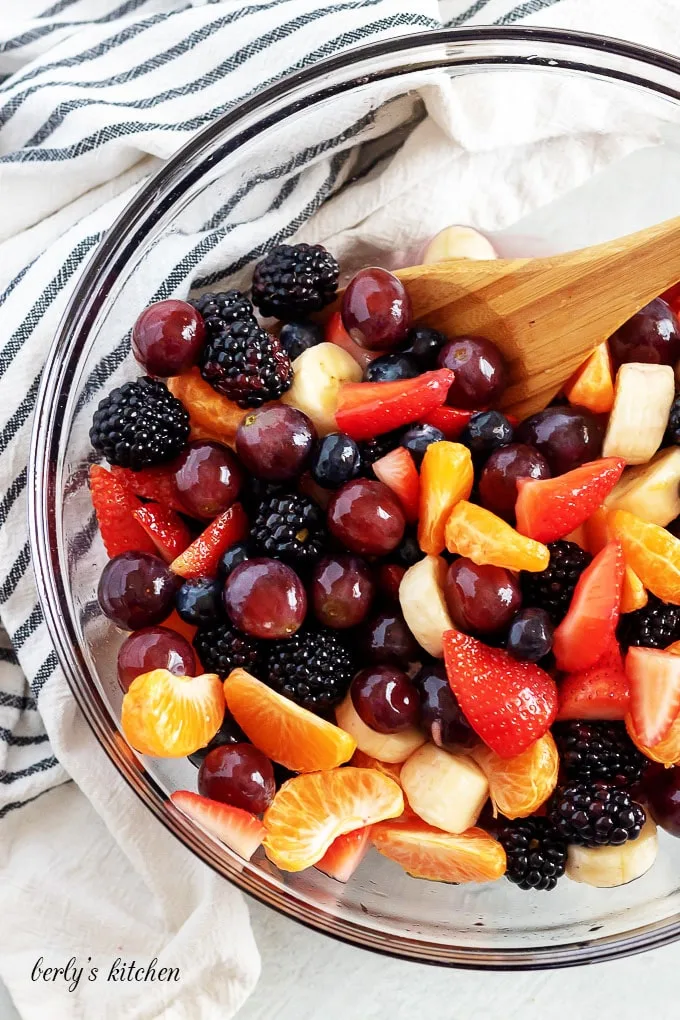 The mixed fruit is being gently tossed with a wooden spoon.