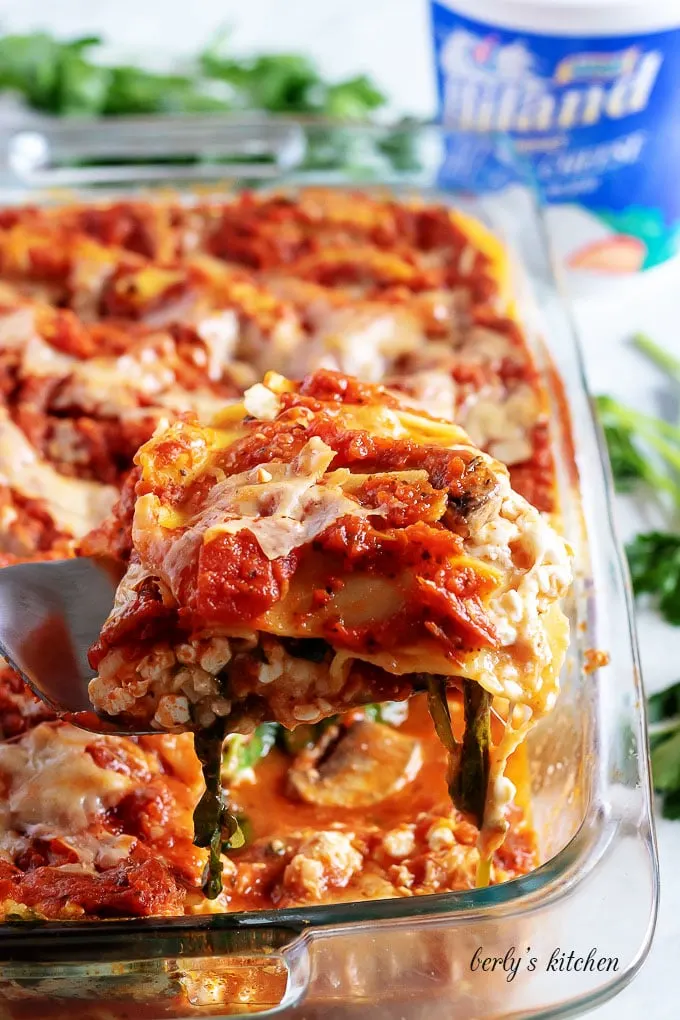 A slice of mushroom lasagna being scooped from the casserole pan.