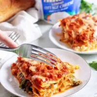 A slice of mushroom lasagna being cut with a fork.