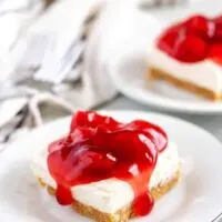 Two cheesecake bars, on white plates, covered with cherry topping.