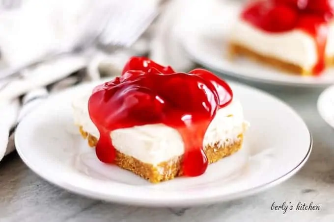 A small square of the cheesecake bars, topped with cherry pie filling.