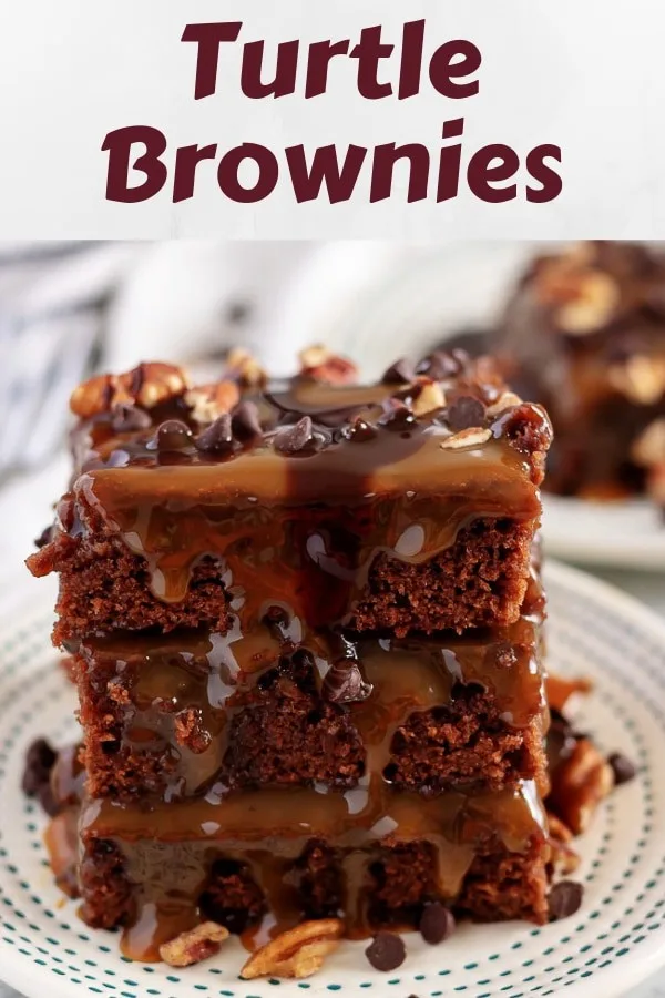 Three turtle brownies covered in caramel and stacked on a white saucer.