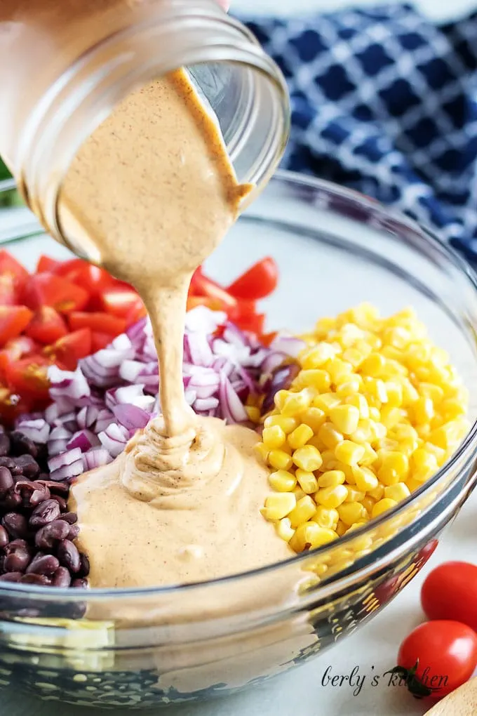 The southwest dressing being poured over the beans, corn, and other ingredients.