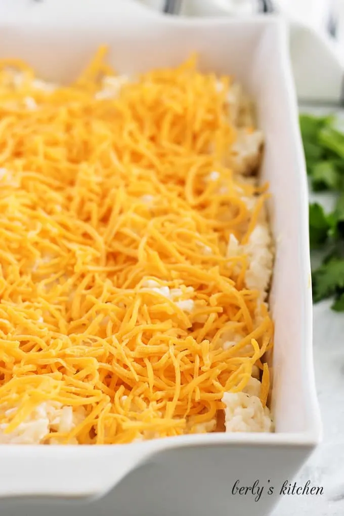 The unbaked casserole mixture, topped with cheddar, in a casserole dish.