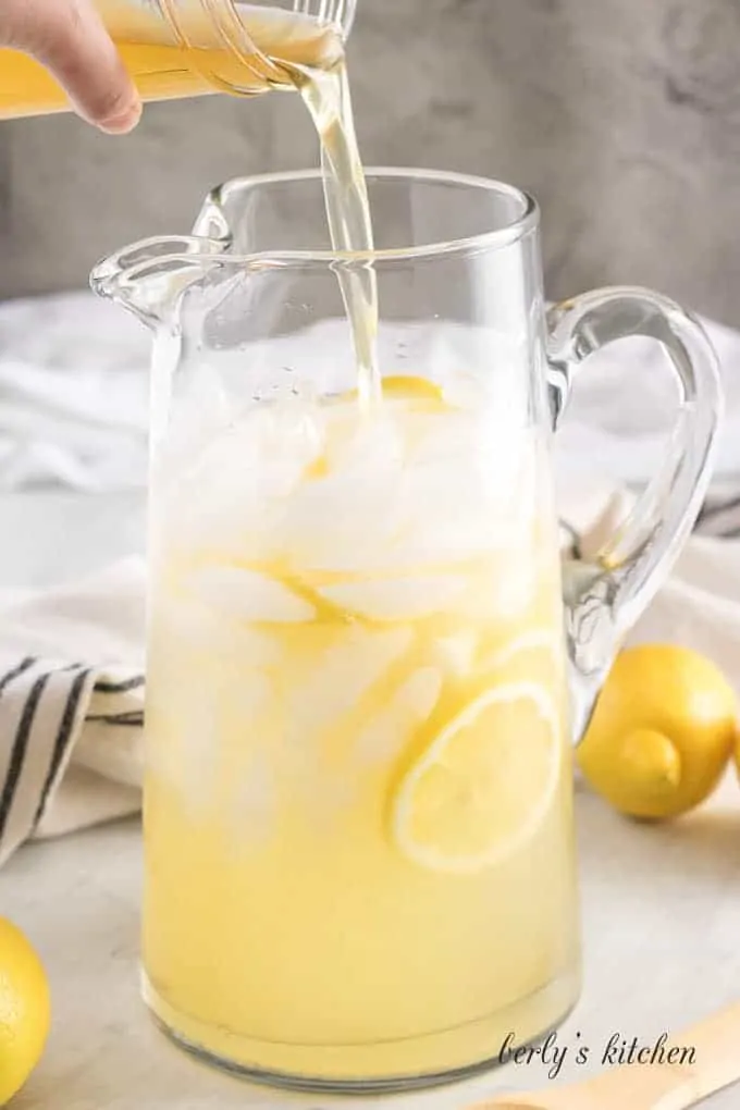 The serving pitcher being filled with the fresh made lemonade.