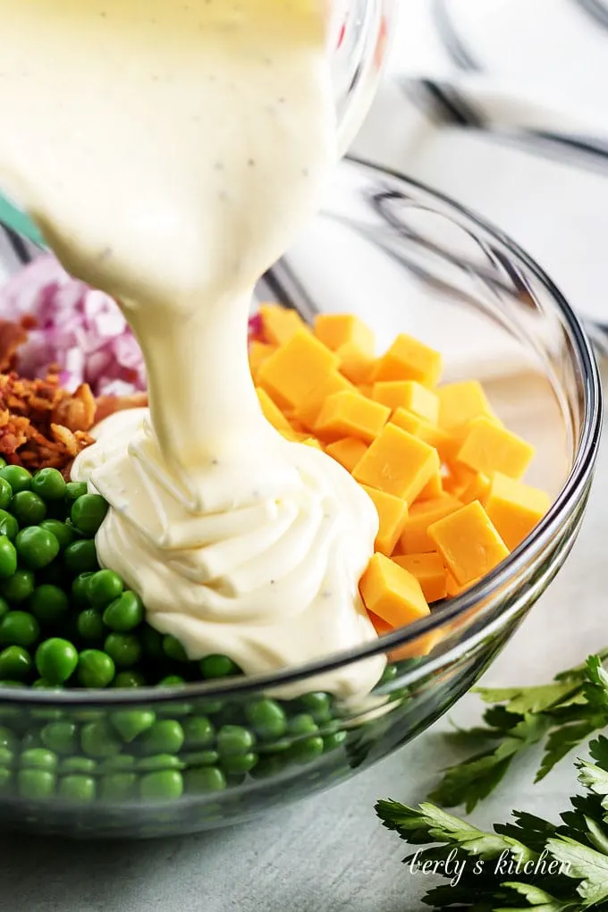 The dressing being slowly poured over the peas and other ingredients.