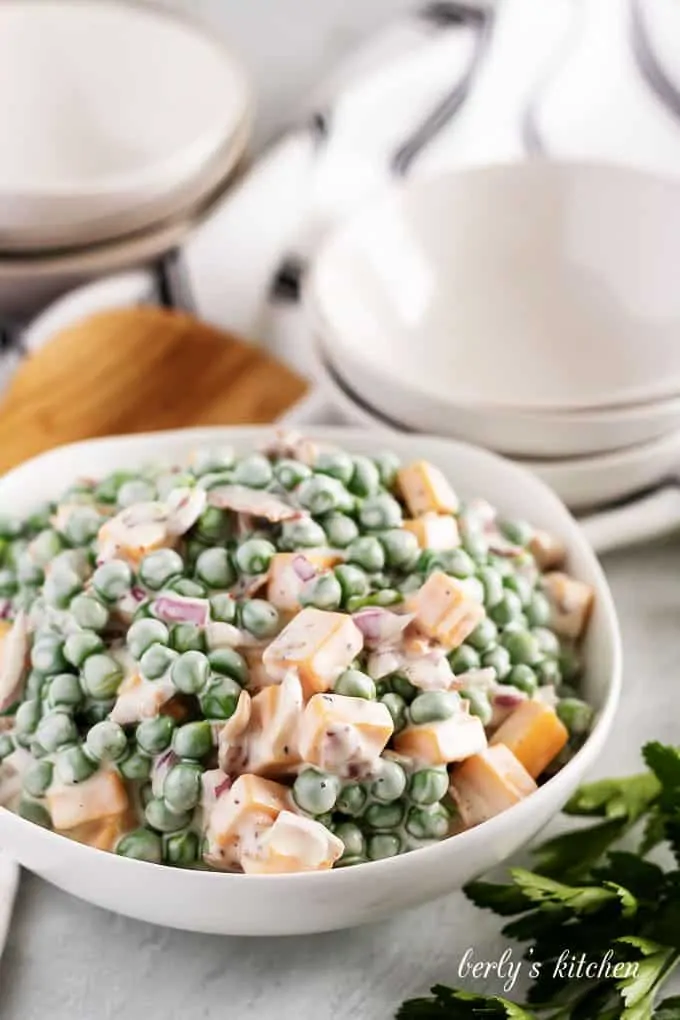 Pea salad in a bowl with cheese and crumbled bacon on top.