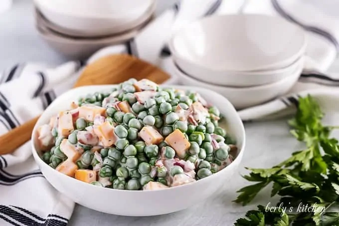 The pea salad served in a large bowl with a wooden spoon.