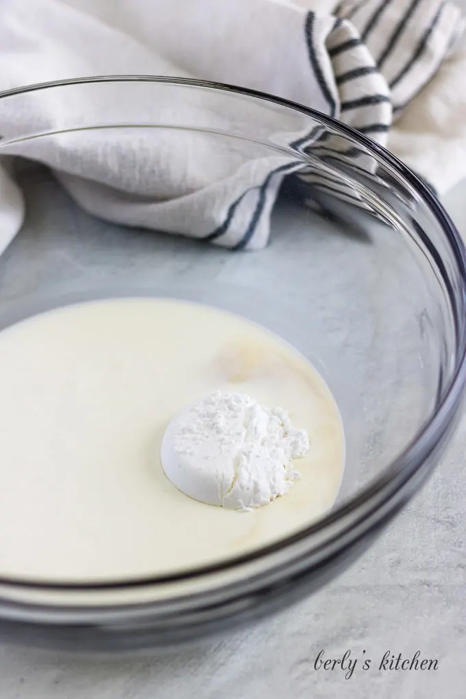 A mixing bowl with the cream, sugar, and vanilla added to it.