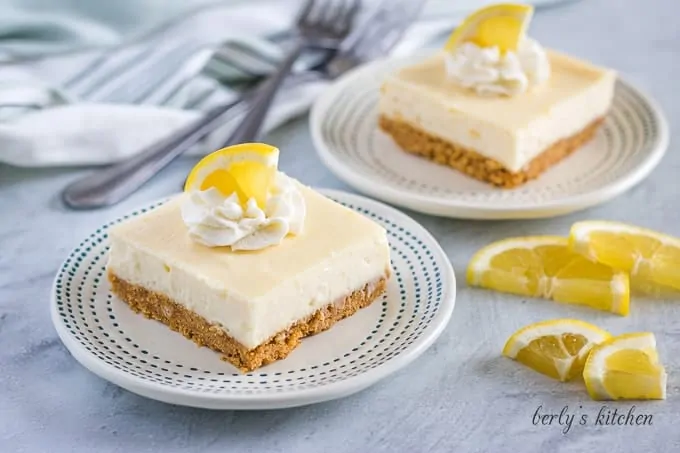 Two squares of the lemon cheesecake bars served on decorative plates.