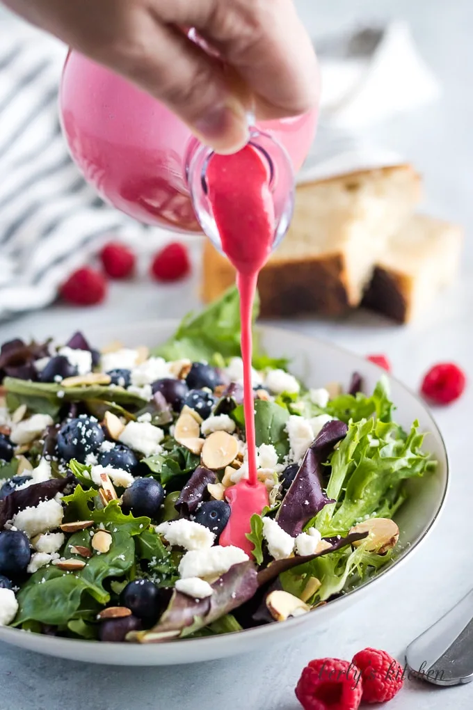 The raspberry vinaigrette being drizzled over a fresh spring mix salad.