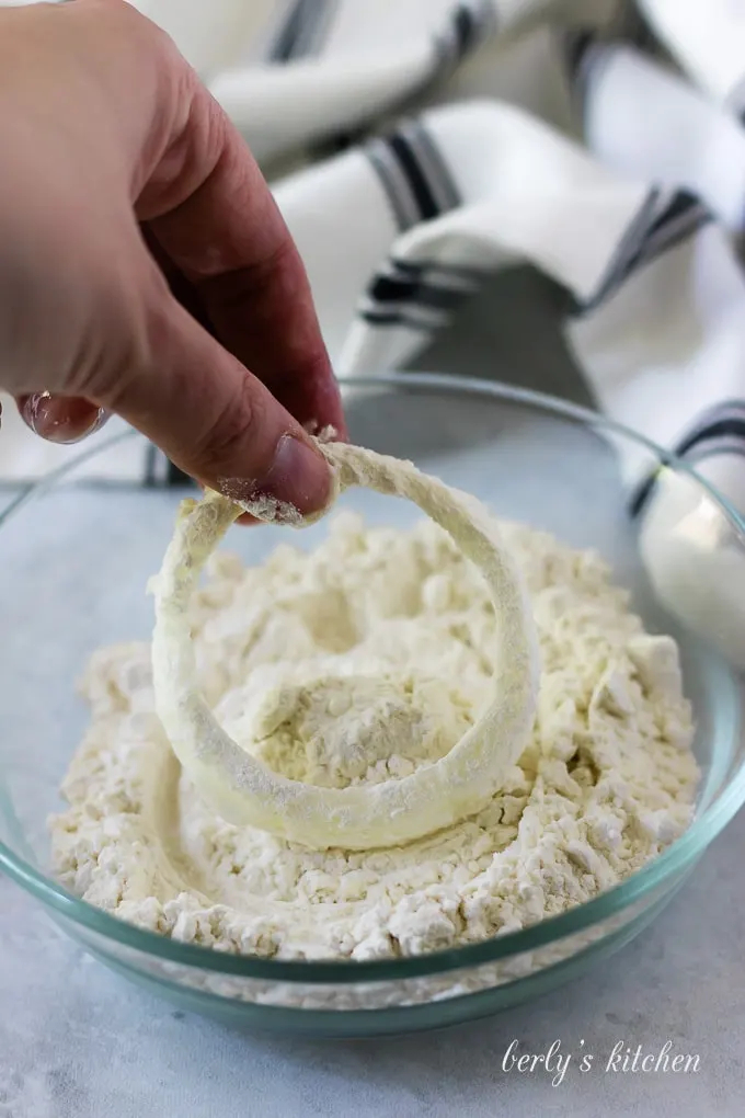 An onion ring being dredged in flour to make the first coat.