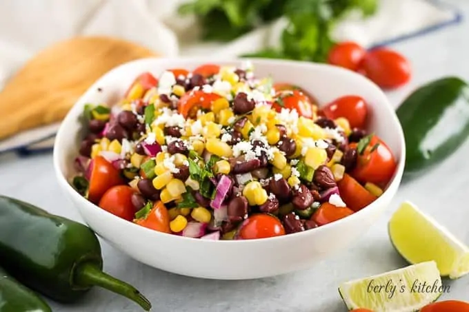 A bowl filled with corn and black bean salsa garnished with limes.