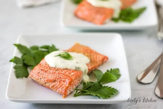 The finished baked salmon topped with dill sauce and garnished with parsley.