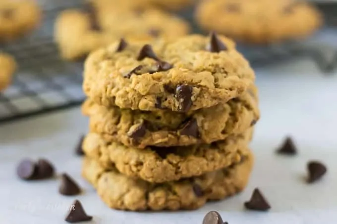 Four stacked oatmeal chocolate chip cookies surrounded by chocolate chips.