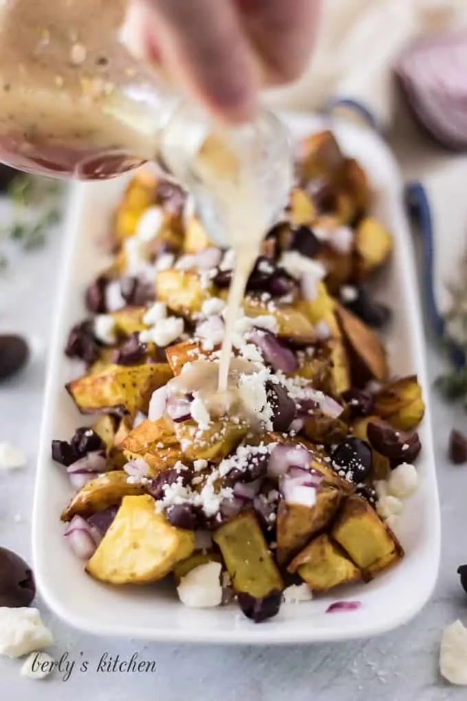 Greek dressing being slowly drizzled over the taters, onions, cheese, and olives.