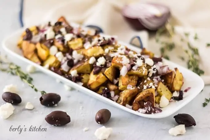 A rectangular plate loaded with greek potatoes topped with feta cheese.