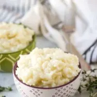 Decorative bowls loaded with instant pot risotto surrounded by herbs.