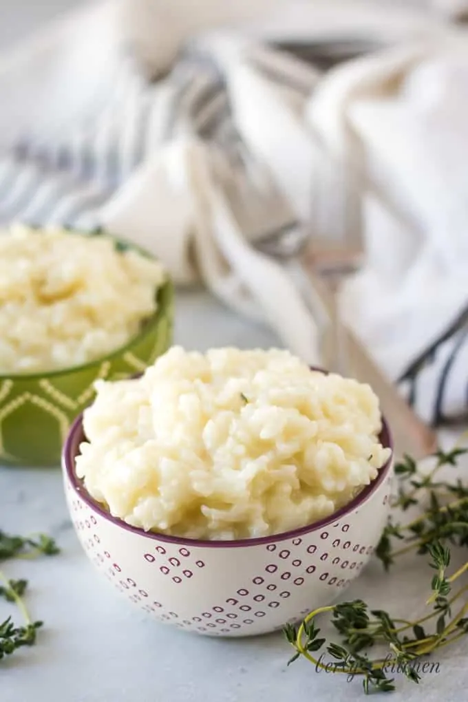 Decorative bowls loaded with instant pot risotto surrounded by herbs.