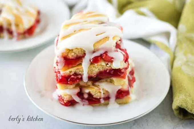 Three cherry bars drizzled with icing stacked on a plate.