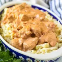 A blue bowl filled with chicken paprikash and cooked spaetzle.