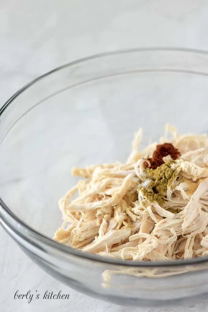 Shredded chicken in a bowl mixed with a blend of spices.